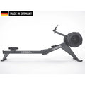 Titanium Strength rowing machine featuring a sleek black design with a built-in digital console, foot pedals, and a durable flywheel. A 'Made in Germany' badge is displayed in the top left corner.