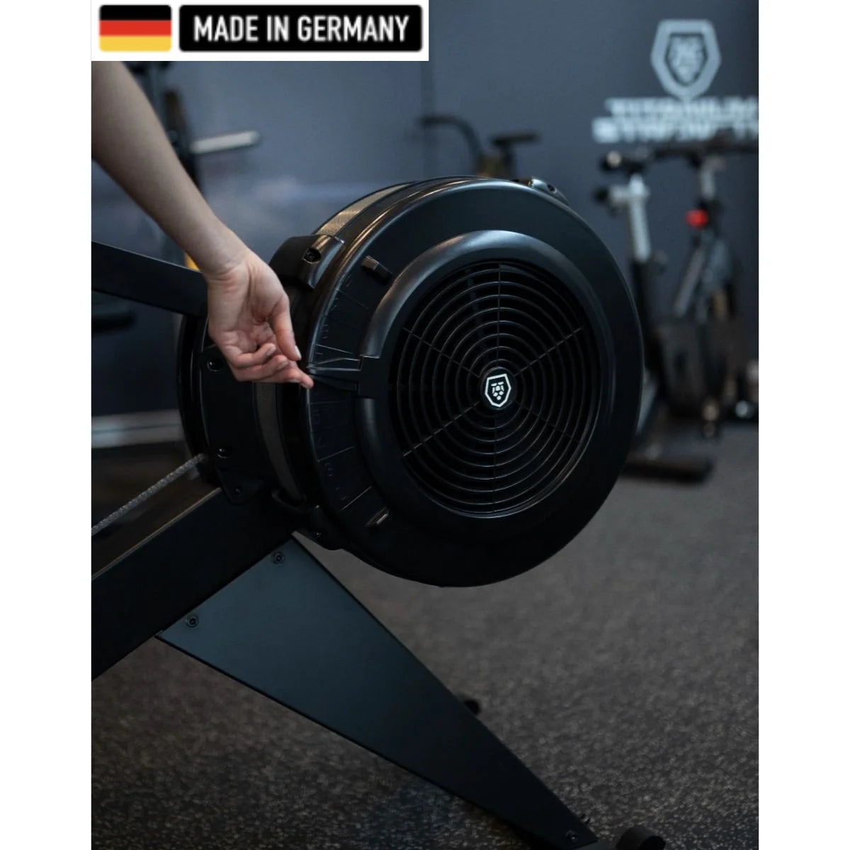 Titanium Strength rowing machine featuring a sleek black design with a built-in digital console, foot pedals, and a durable flywheel. A 'Made in Germany' badge is displayed in the top left corner.